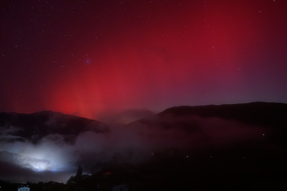 Reddish auroras in a starry sky. In the foreground, the village of Kartitisch (East Tyrol) at night.