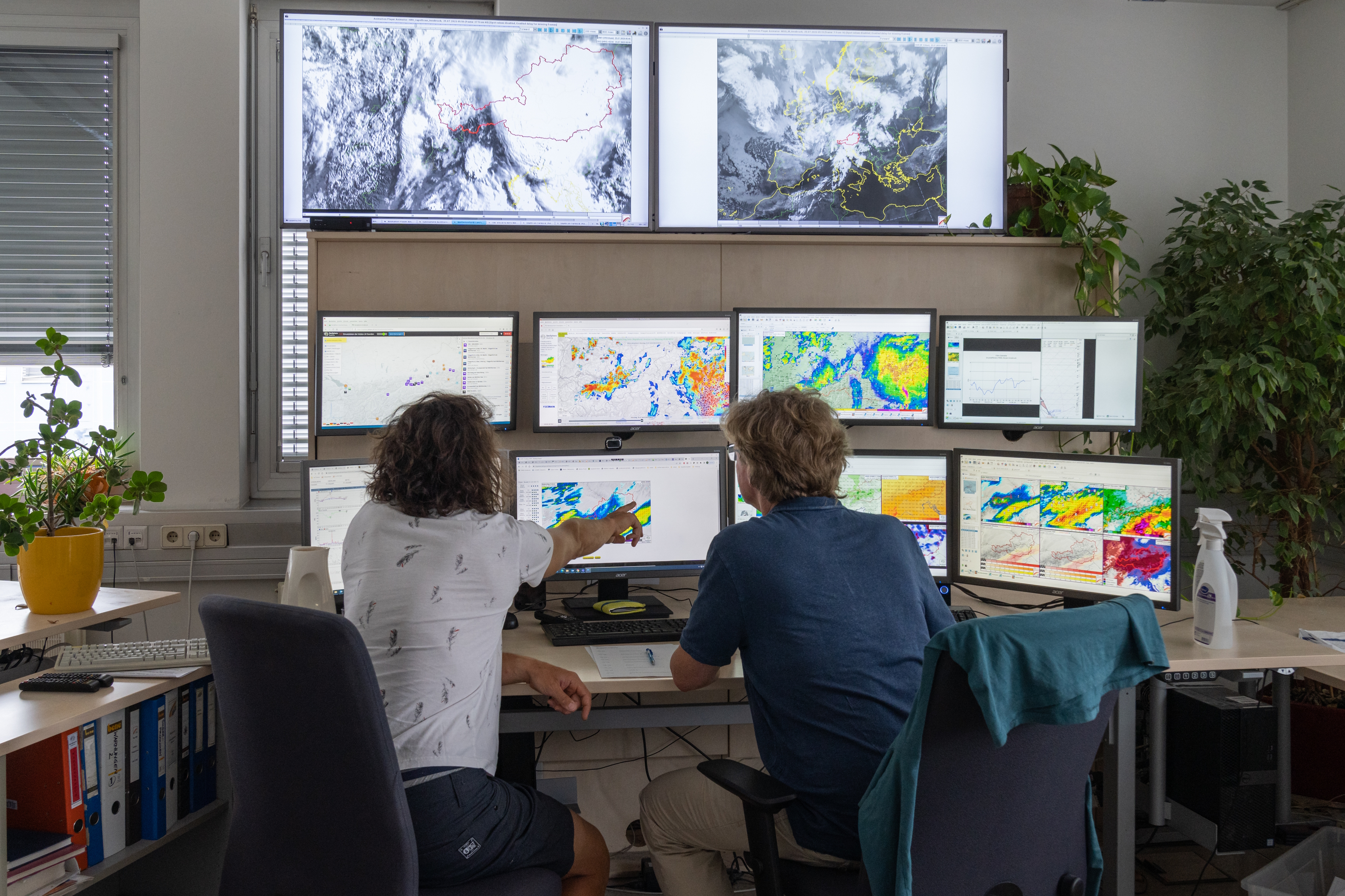 Two people sit in front of 8 screens.